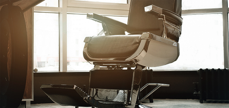 Vintage barber chair in a sunlit room with large windows, casting soft shadows. The leather upholstery and metal details evoke a nostalgic atmosphere.